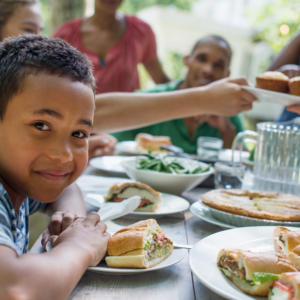 healthy family eating sandwiches together. a young child smiles at the camera