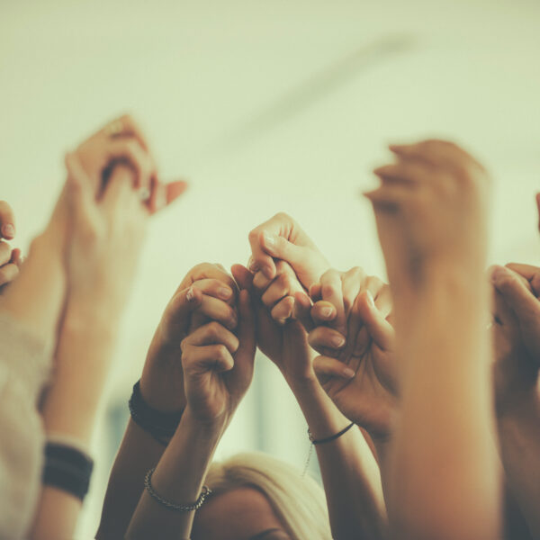 a group of people stand together with their hands joined and raised above their heads. practice compassion