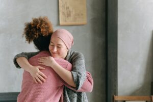 two people gently hug. One is wearing a pink scarf covering her head