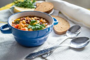 hearty soup in a ceramic bowl next to spoons and slices of bread. how to package soup for meal train