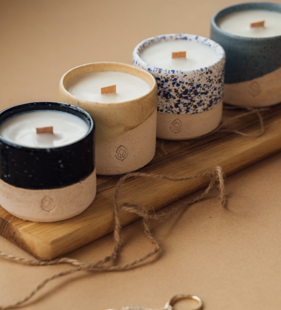 bamboo-wick candles in small, decorative ceramic pots lined up on a wooden board. what to get someone with a new house