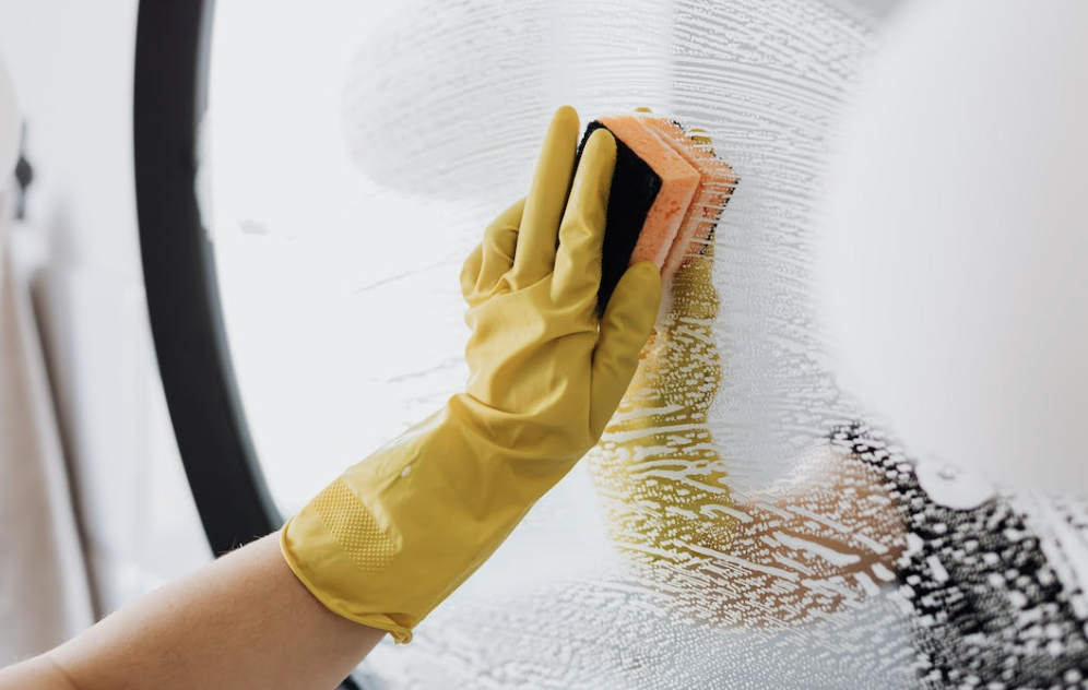 person in yellow gloves scrubbing a mirror