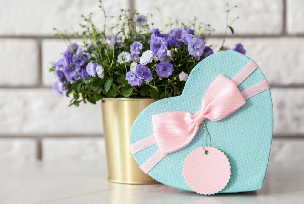 blue box of chocolates with a pink bow and purple flowers in a gold pot