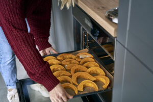 Close up of woman putting pumpkin to oven at home