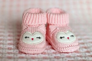 Pink, knit, baby booties with facial features and pointy ears embroidered on. Homemade baby clothes and blankets are great DIY meal train ideas for new parents.
