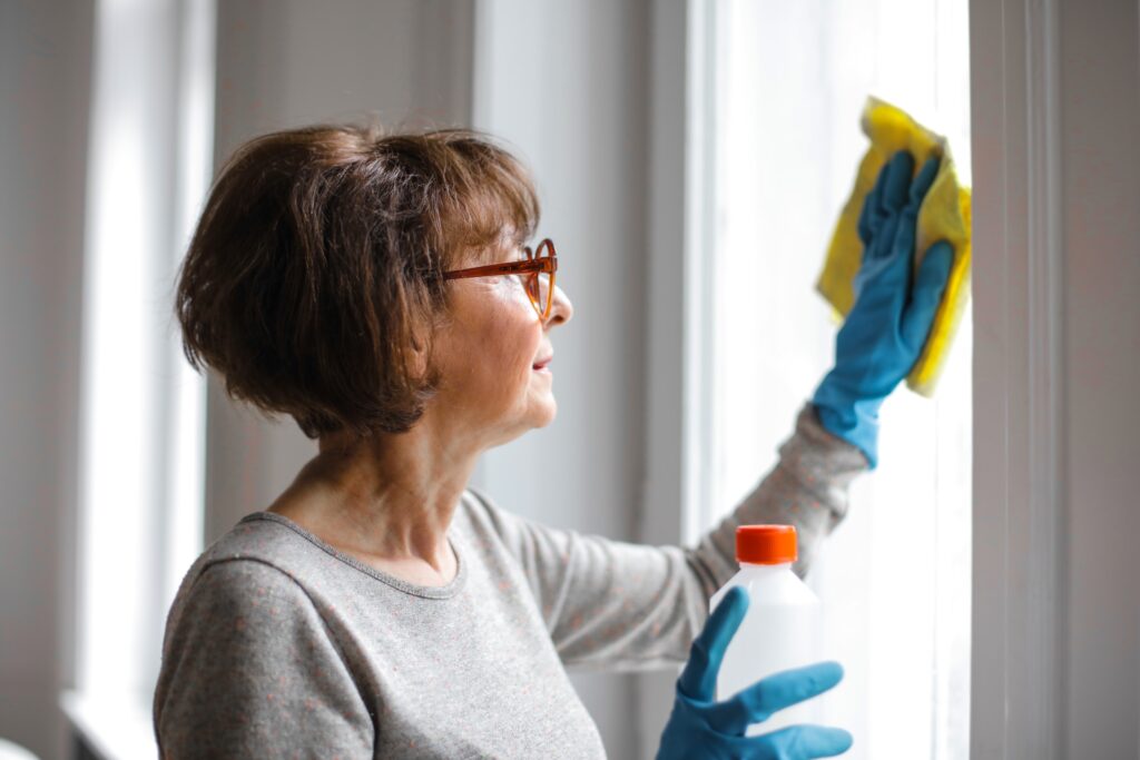 woman wearing protective gloves washing a window with cleanser and a cloth