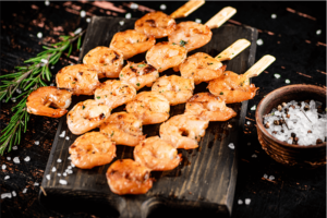 Grilled shrimp on skewers lay on a rustic wooden board. great summer meal train ideas