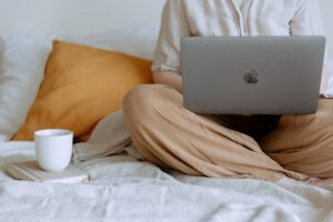 Person in bed with a beverage in a mug on a coaster and holding a laptop computer in their lap.