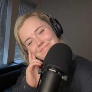 Alex Alexander wears headphones and smiles in front of her podcast microphone